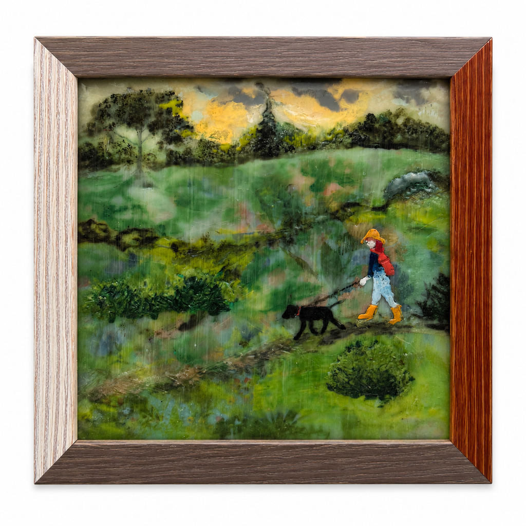 Original encaustic painting of a figure in a yellow wide-brimmed hat, red jacket, and yellow rubber boots walking a black dog through a lush green landscape under a dramatic stormy gold and grey sky. Rain falls across the entire composition. Professionally framed in two-tone wood. 9 x 9 inches. By Marilyn Clayton, 8th by MOC Designs.
