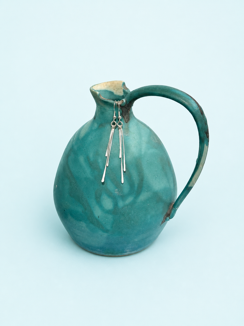 Three hand-hammered sterling silver paddle drop earrings on a light teal mineral background, graduated lengths, French hook ear wire